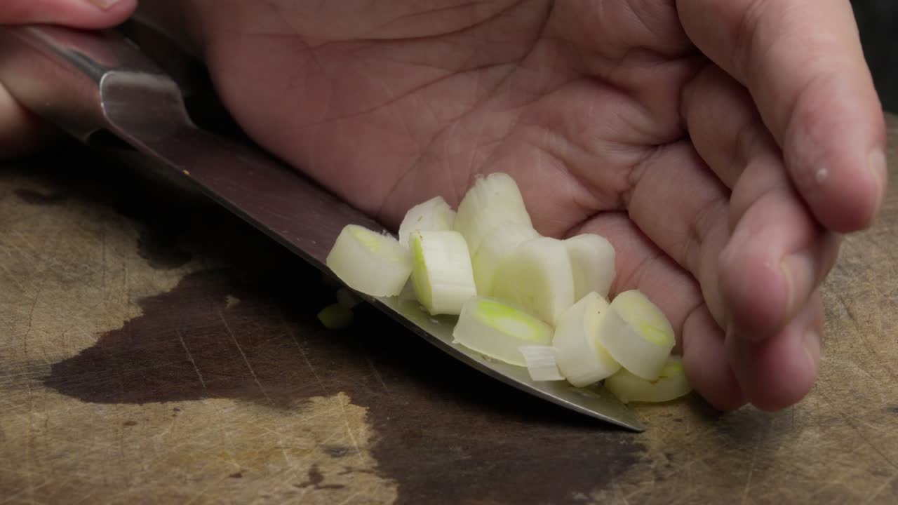 Close-up of a knife swiping chopped onion on a wooden board