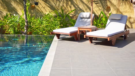 pair of chaise-longues under parasol near swimming pool border at private house in bali