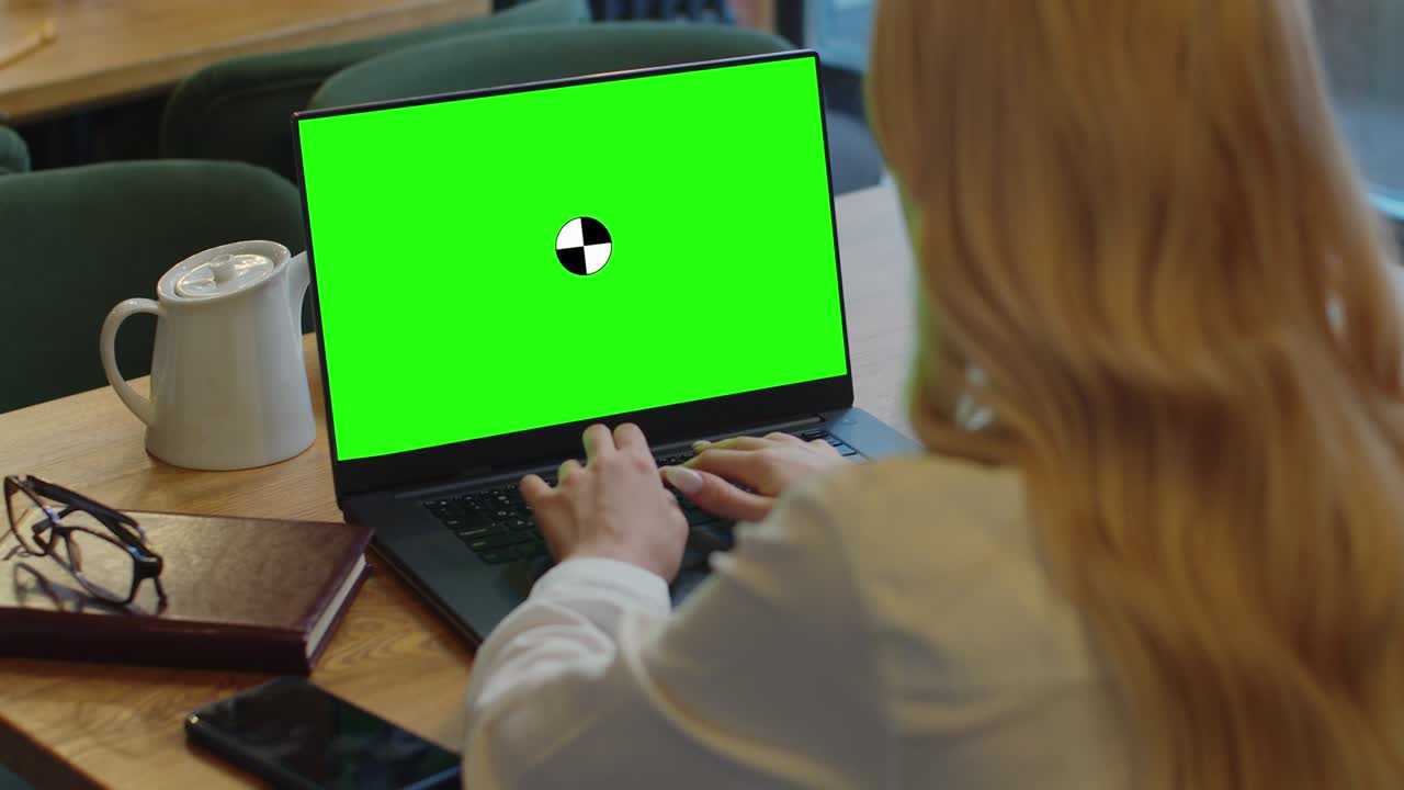 una mujer usando su portátil con pantalla verde en blanco y escribiendo. sentada en un café y bebiendo café.