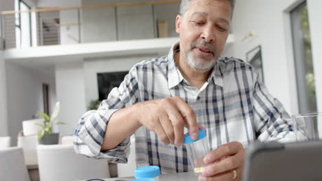 senior biracial man with medication having video call on tablet with doctor, slow motion