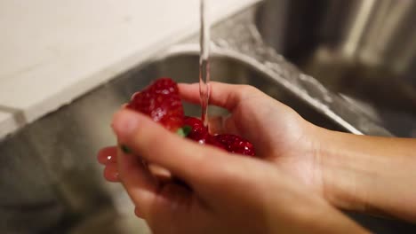 hands washing strawberries under a kitchen faucet