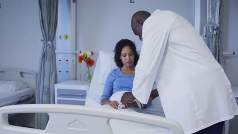 Diverse-male-doctor-putting-female-patient-on-drip-in-hospital-room