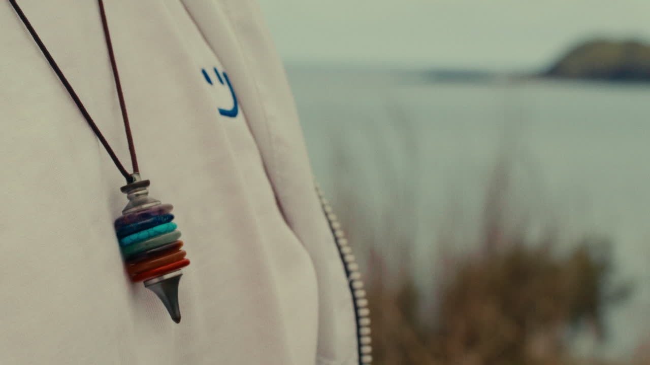 Close-up of a necklace with a colorful stone pendant and a view of the ocean