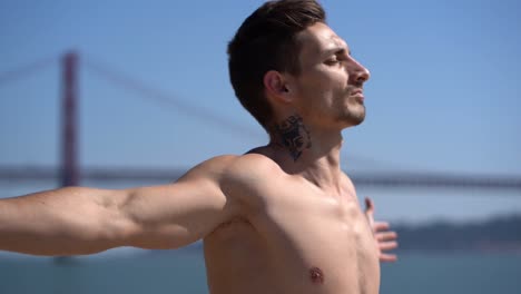 Muscular-shirtless-man-standing-with-open-arms-against-blue-sky