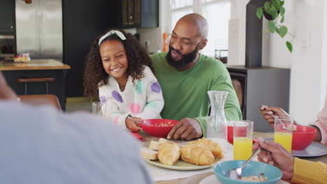 video of happy african american daughter laughing and feeding father at family breakfast table