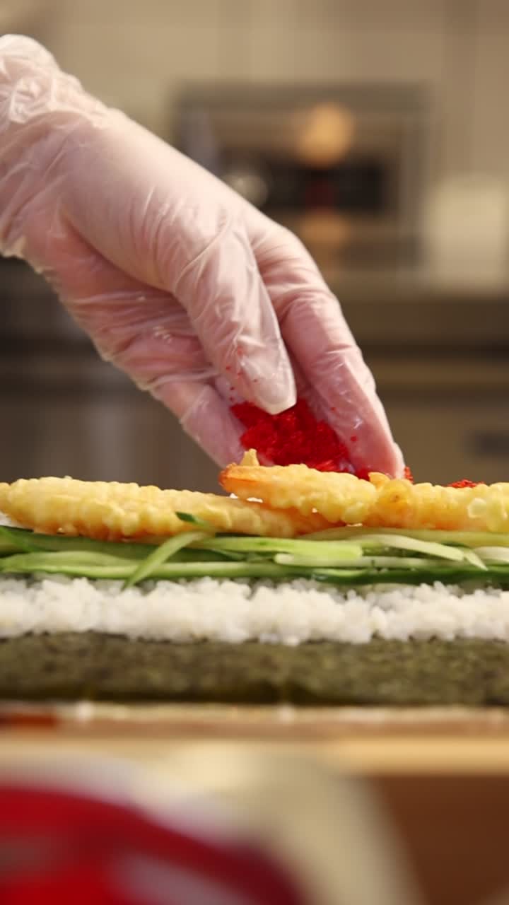Chef's Hand in Glove Sprinkling Red Roe on a Sushi Roll