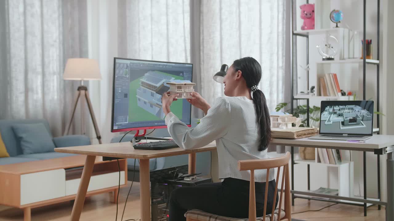 Ingegnere donna asiatica che tiene in mano e guarda il modellino di casa con pannello solare mentre progetta una casa su un desktop a casa. Design e decorazione di case per videogiochi