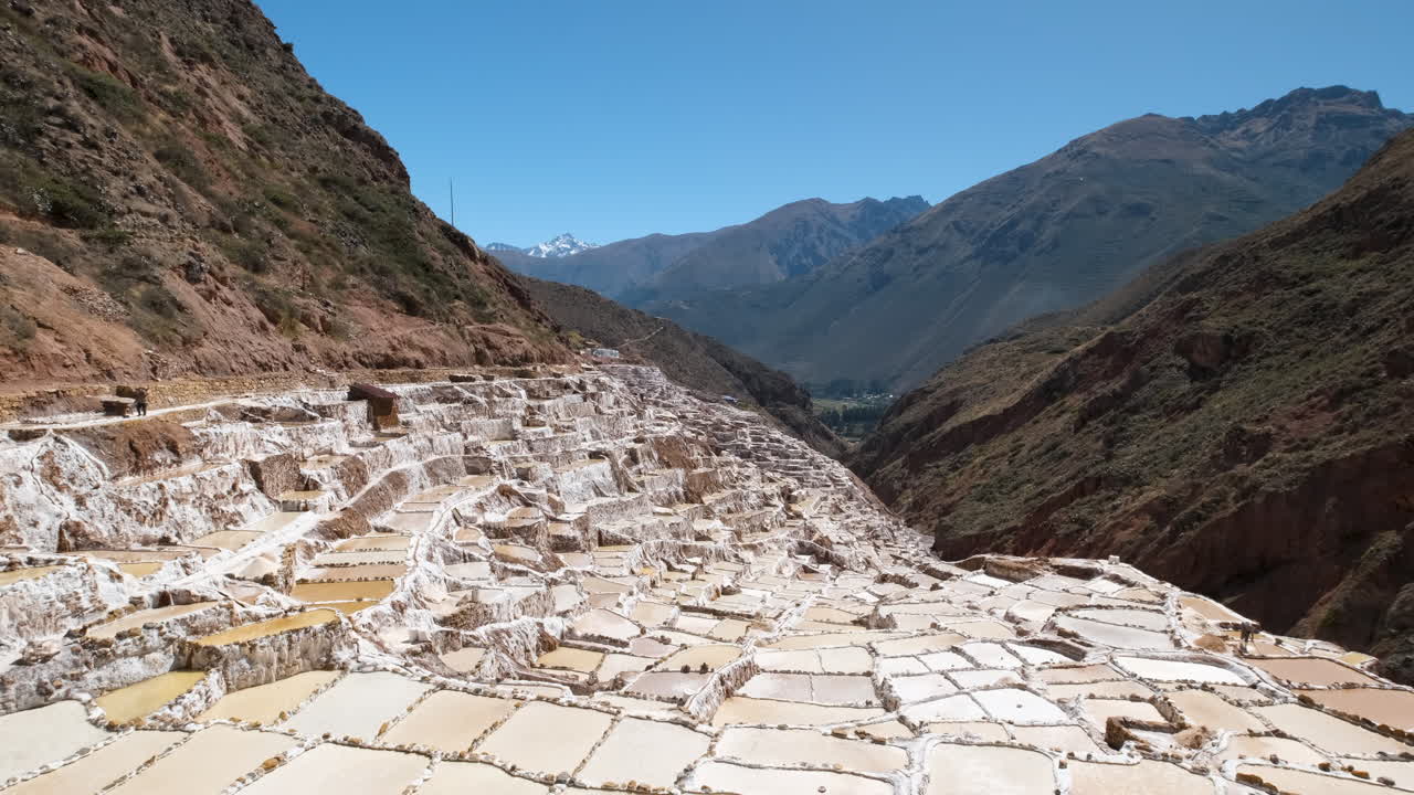 Pan shot showcases the vast Maras Salt Pans, a unique natural and historical marvel nestled within Peru's Sacred Valley. Witness the incredible terraced salt pools against a dramatic Andean