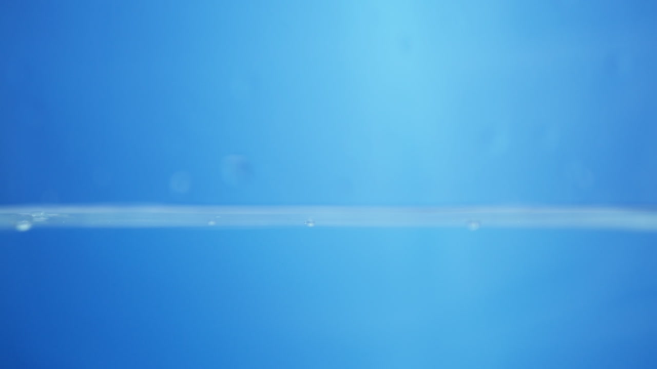 Close-up of water droplets splashing in slow motion, showing purity and transparency in a macro view of fluid motion. Ideal for spa or fresh concepts.