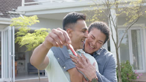 portrait of happy diverse gay male couple with new house keys embracing in garden, slow motion