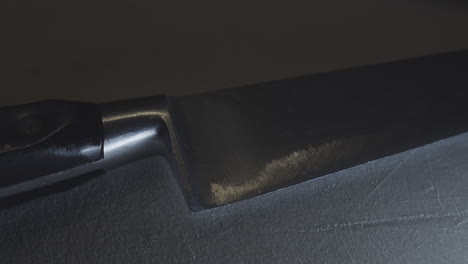 dramatic close-up of knife edge on stone surface, slow motion