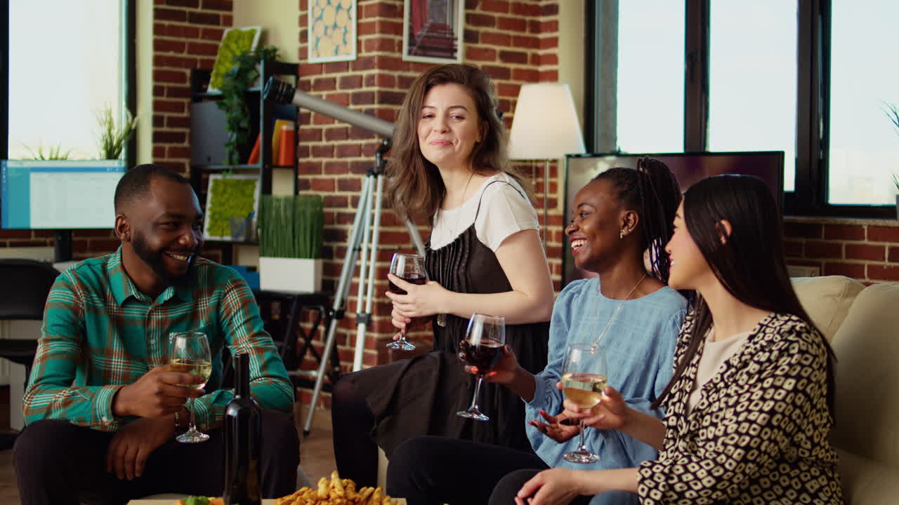 Multicultural friends having fun together, enjoying alcohol drinks and snacks in cozy living room
