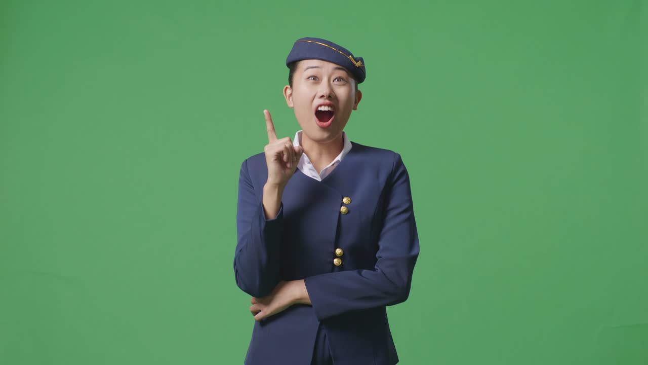 아시아 여성 승무원이 생각하고 주위를 둘러보며 녹색 스크린 배경 스튜디오에 서있는 동안 지표손가락을 들어 올립니다.