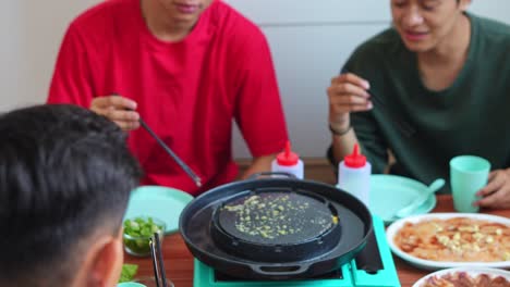 group of young asian men gather around table enjoying casual homemade meal cooked on portable grill