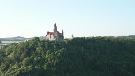 aerial view of the majestic bouzov castle standing on top of a forested hill