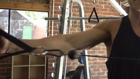 hombre musculoso en el gimnasio en casa ejerciendo un solo brazo con cable de oscilación del hombro