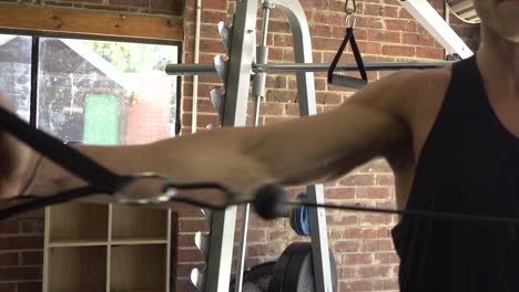 muscly man in home gym exercising single arm cable shoulder swing