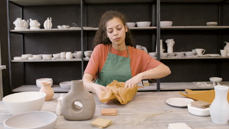 mujer joven envolviendo cerámica artesanal con papel mientras se sienta a la mesa en la tienda de cerámica