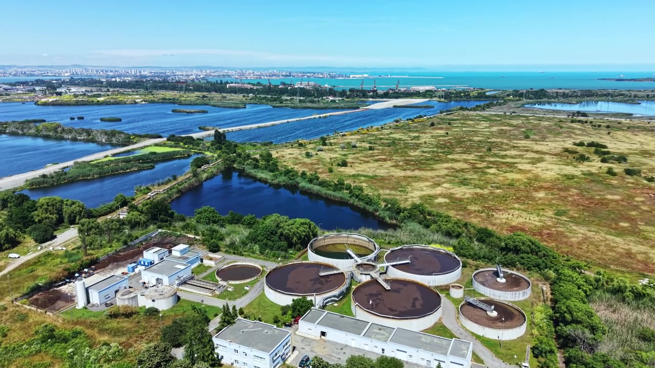 Impianto di trattamento dell'acqua situato in una zona costiera, circondato da campi, fiumi e pannelli solari in una giornata di sole.