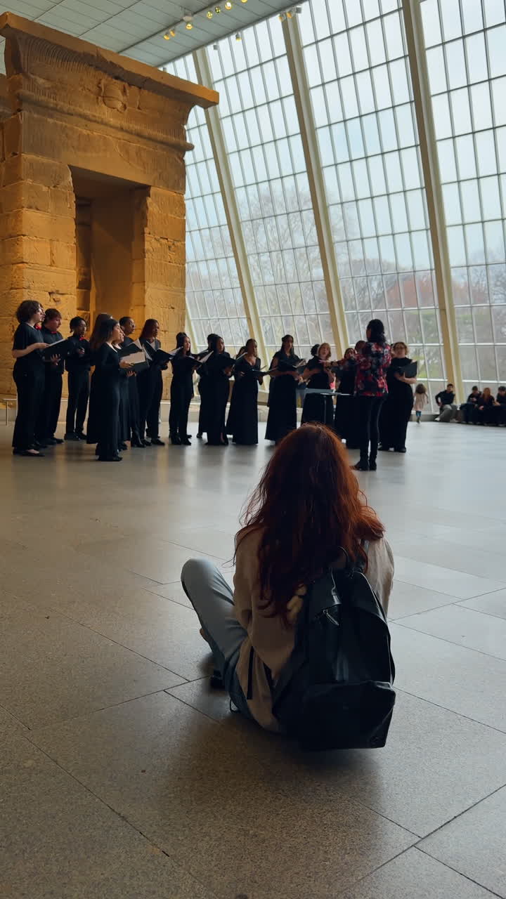 New York, AS, 2 Maret 2026: Penonton duduk di lantai mendengarkan paduan suara di aula museum. Orang muda ber ransel menonton pertunjukan grup vokal di depan jendela besar di New York.