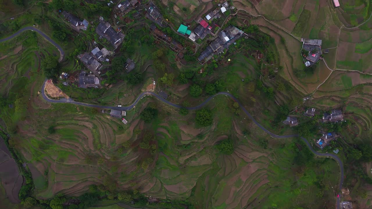 Aerial drone shot of a peaceful village perched on a mountainside surrounded by lush greenery.