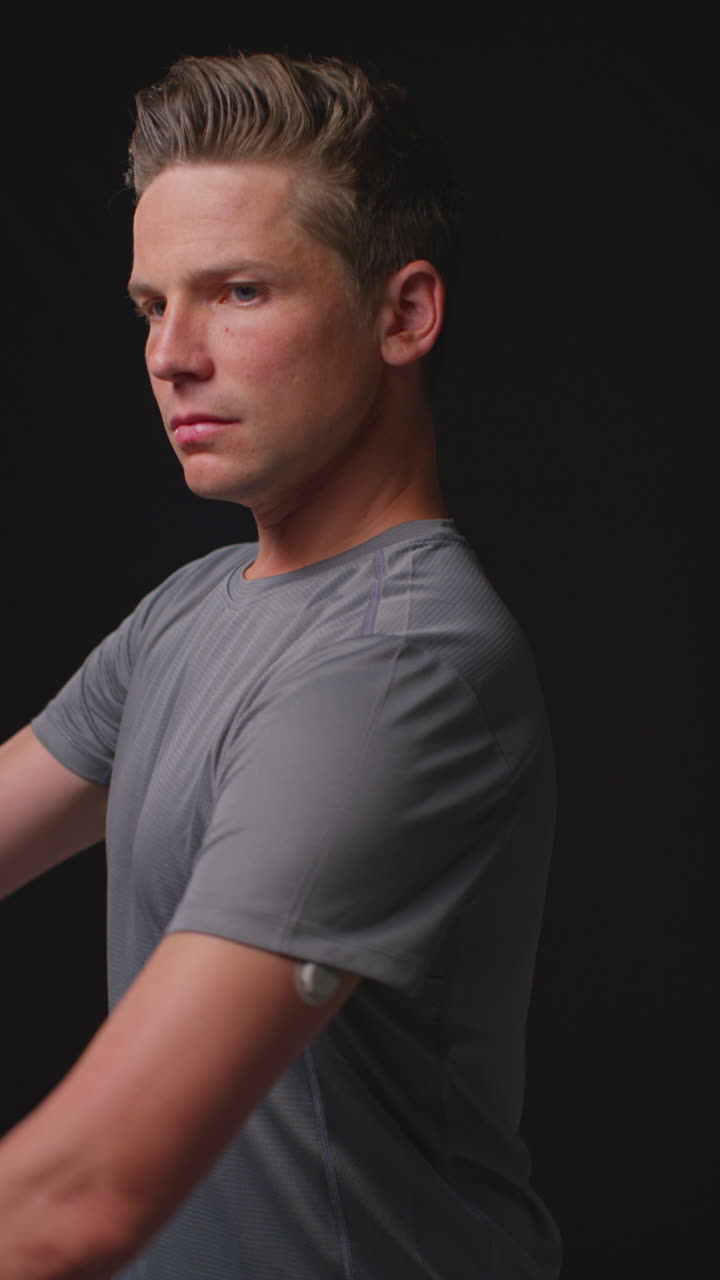 검은색 스튜디오 배경에 대한 스포츠 이벤트를 위해 심리적으로 준비하고 체육 의류를 입고 훈련하는 심각한 남성 운동 선수의 수직 비디오 초상화