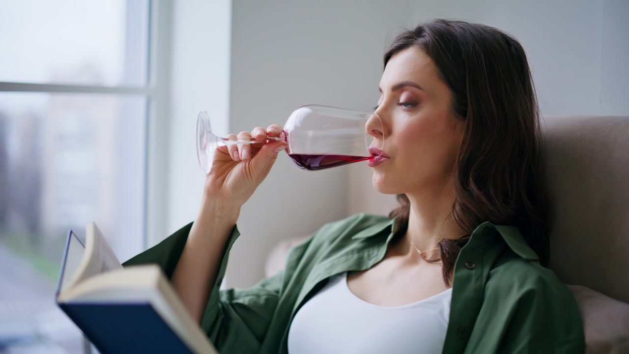 Relaxed reader drinking wine sitting home alone closeup. Woman reading book