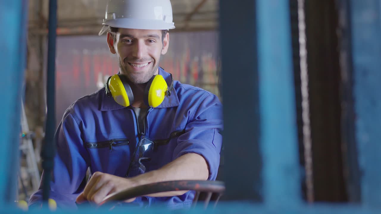 Autista caucasico di carrello elevatore concentrato che aziona la macchina e tiene la mano sul volante, comunicando via radio per il lavoro di squadra nel trasporto di merci in un magazzino industriale.