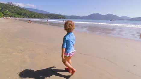 young 4 year old cute girl running freely on the beach with mountains background and calm sea and clear sand