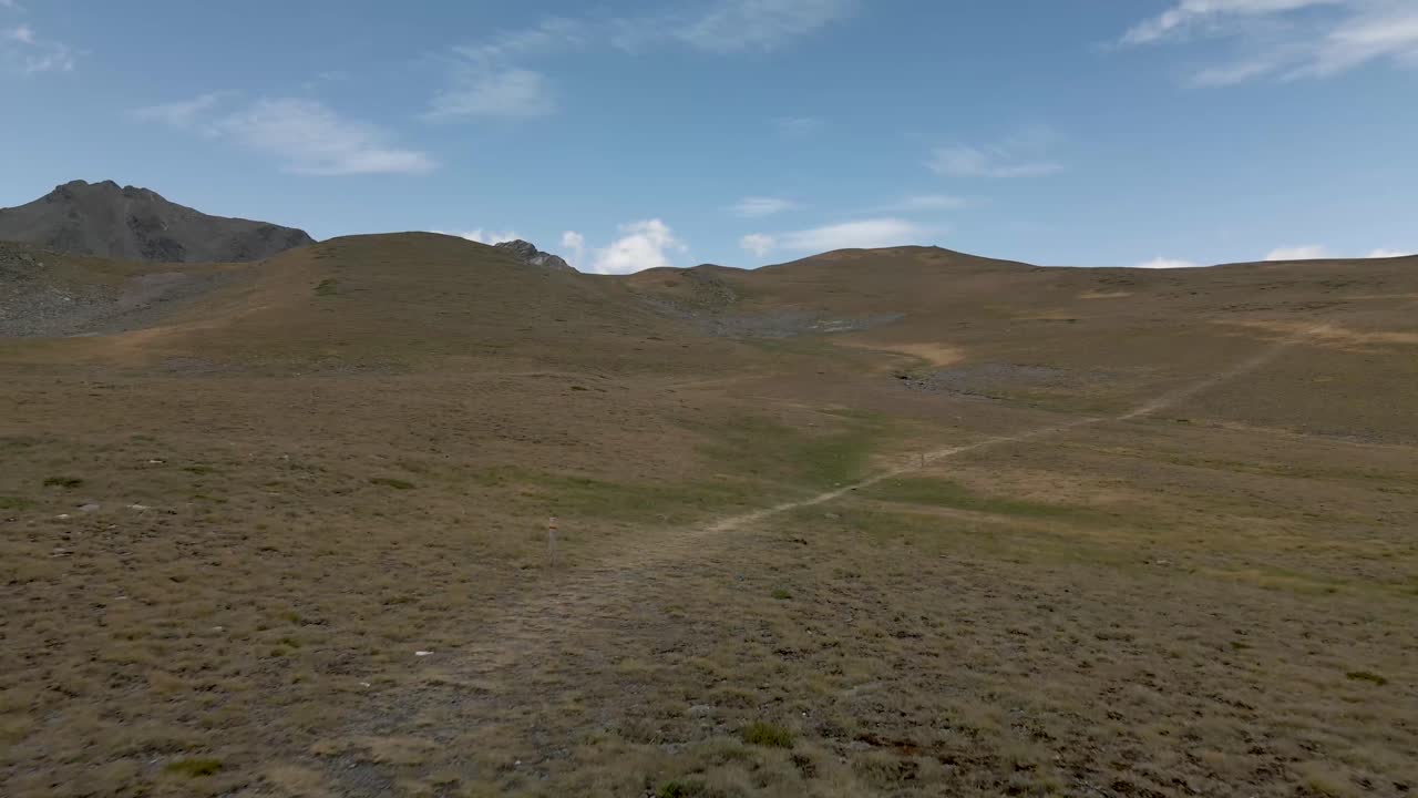 Veduta aerea da drone che avanza attraverso i campi di montagna seguendo il sentiero pedonale