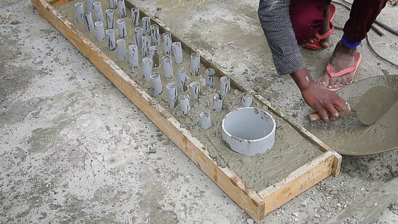 Indian mason worker placing and leveling wet concrete mix in the slab around the pipes for construction