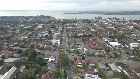 Aerial-view-of-intersection-with-busy-car-traffic-in-the-residential-area,-houses-or-home-and-ocean-in-the-horizon