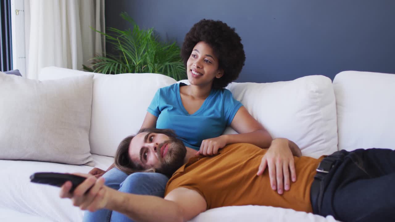 pareja de raza mixta viendo televisión juntos en el sofá en casa