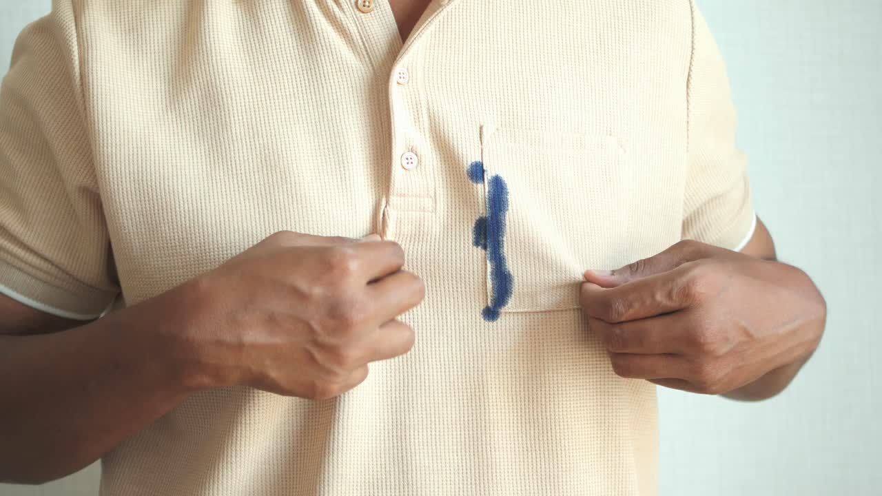 un uomo indica una macchia di inchiostro blu sulla tasca della sua camicia.
