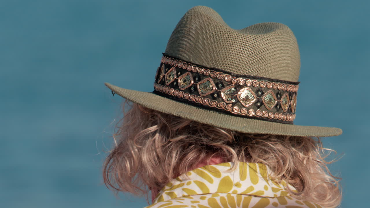 Close up of a decorated sun hat worn by a person facing the calm blue water