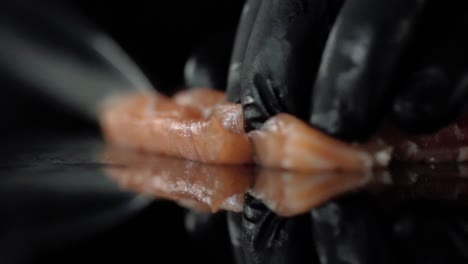 a person wearing a black glove cuts a piece of salmon sashimi with a knife