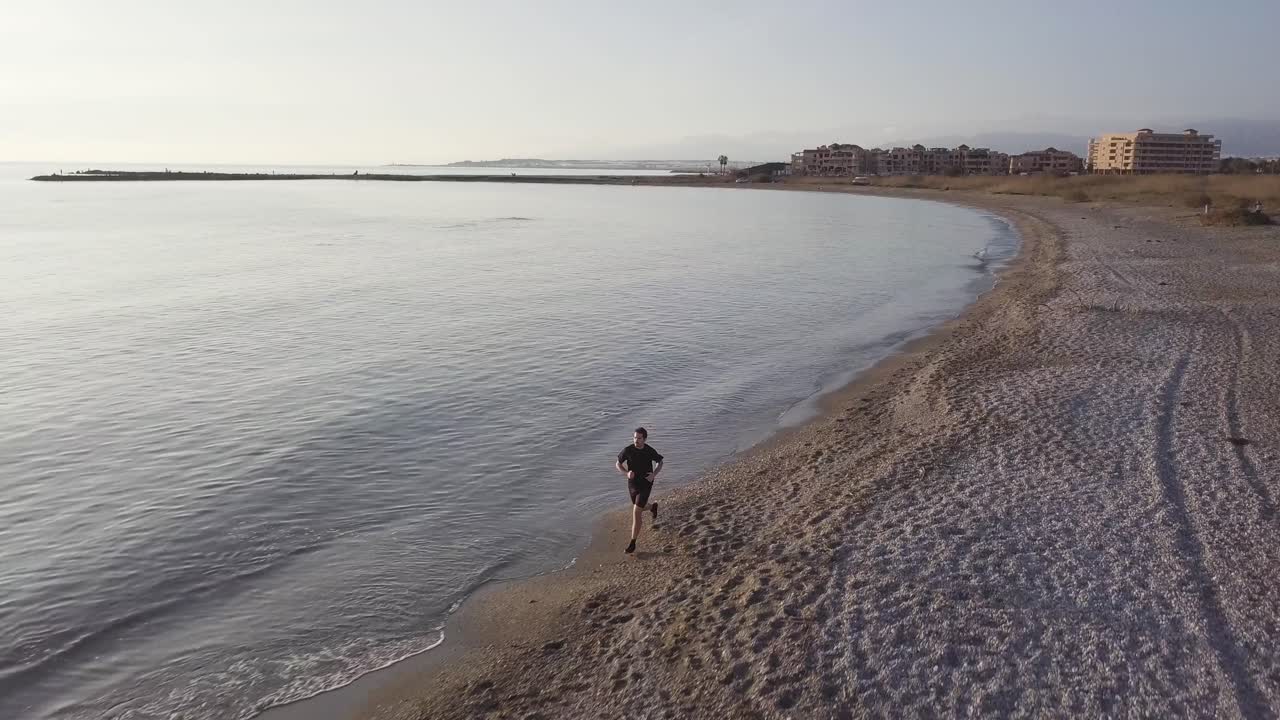 Young runner man training on beautiful sunset at beach. Drone view