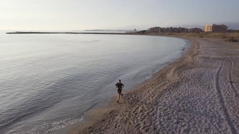 young runner man training on beautiful sunset at beach. drone view