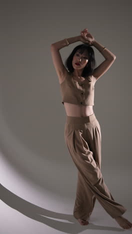 vertical video: model in stylish beige outfit posing confidently in modern fashion studio