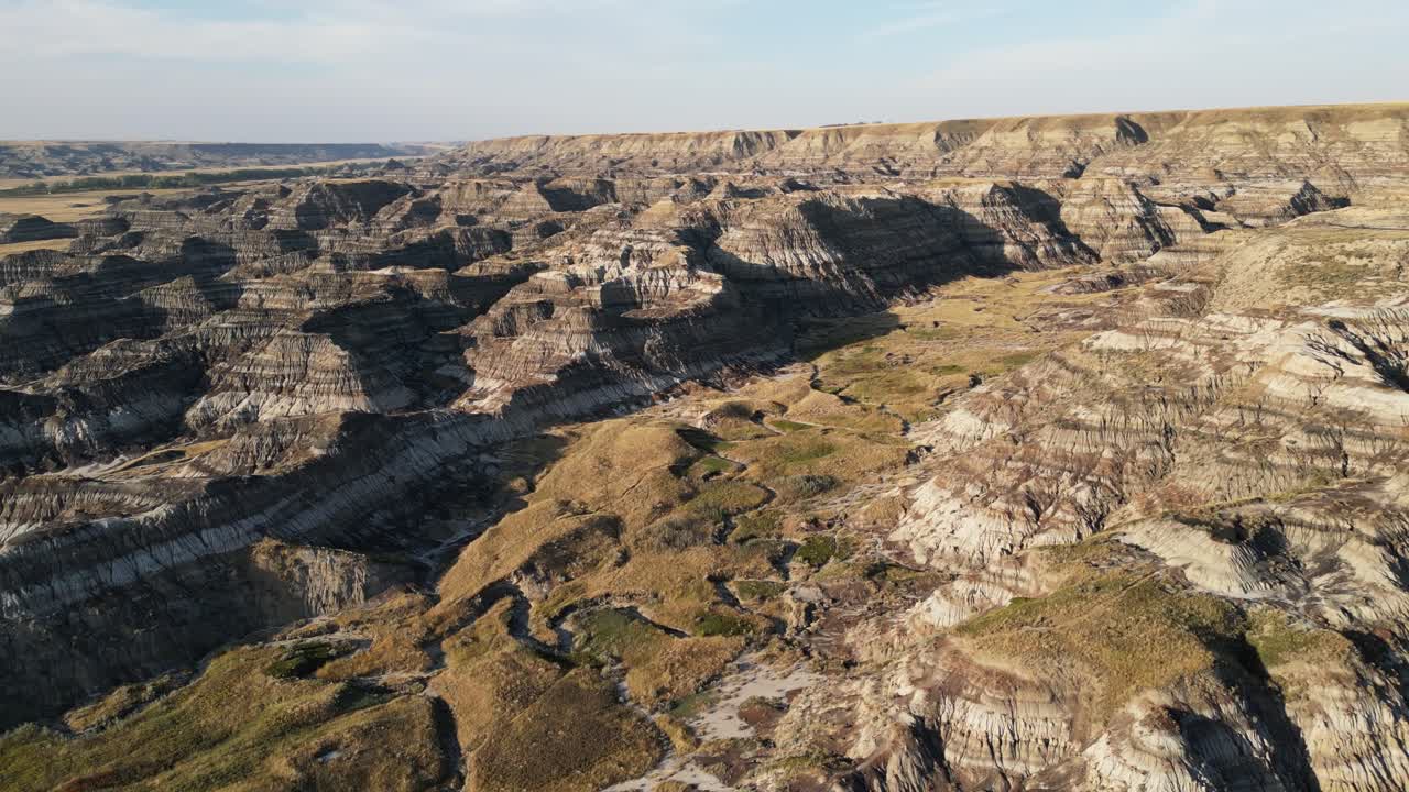 Drone aerial view of badlands hills and a dry riverbed, filmed just before sunset with soft low light and long shadows