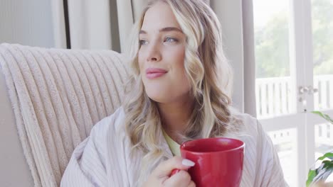 portrait of happy caucasian plus size woman sitting on armchair and drinking coffee in slow motion