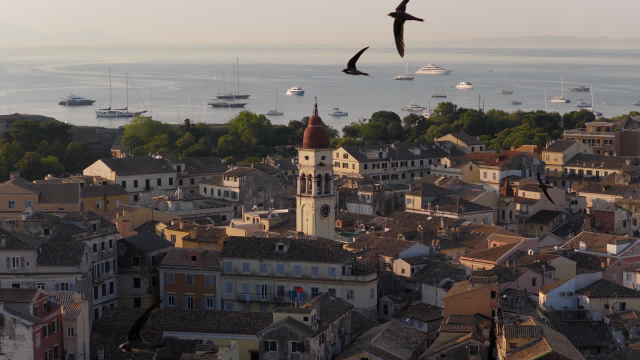 Saint Spyridon Church at sunrise with swallows flying through Old Town Corfu rooftops, drone orbit