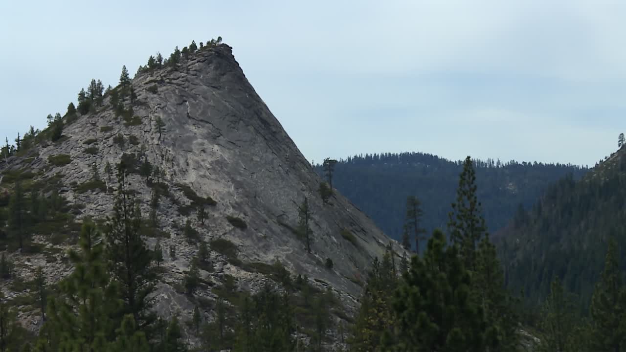 Granite mountain peak with scattered pine trees rising above forest in Eldorado National Forest, California