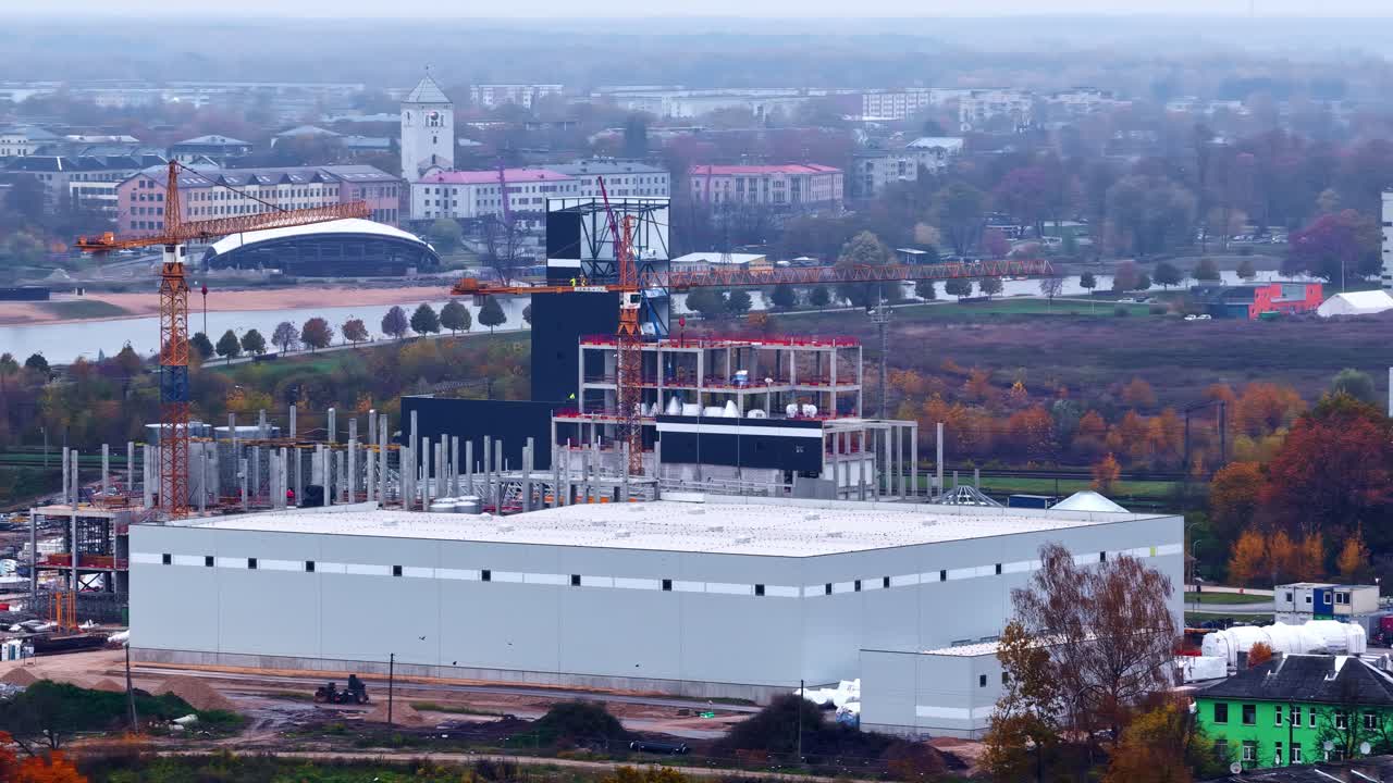 Grande edificio industriale in costruzione con gru e sfondo della città autunnale in vista aerea