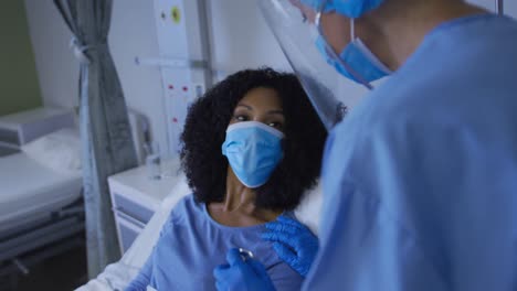 Diverse-female-doctor-and-patient-wearing-face-masks-during-heart-examination