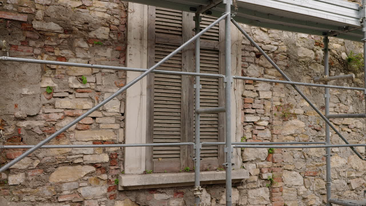 Vecchio muro in pietra con finestra con persiane in legno e impalcatura metallica durante il restauro di un edificio in Italia