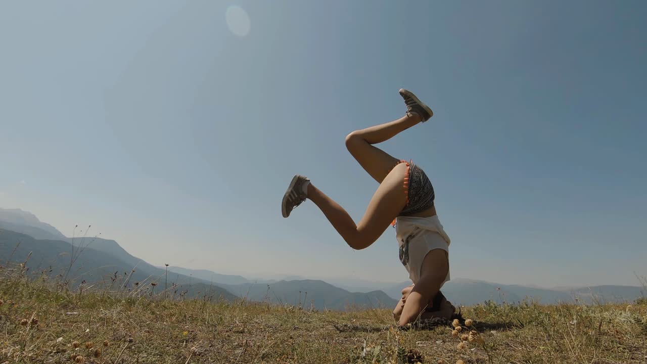 niña tratando de hacer una parada de cabeza de yoga en una montaña, en un día soleado