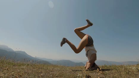 Junges-Mädchen,-Das-Versucht,-An-Einem-Sonnigen-Tag-Einen-Yoga-Kopfstand-Auf-Einem-Berg-Zu-Machen