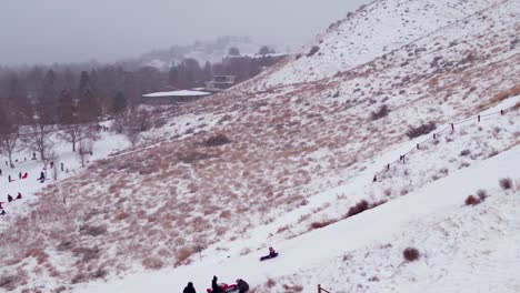 Tiro-Ajustado-De-Un-Dron-De-Un-Niño-Bajando-En-Trineo-Por-Una-Colina-Nevada-En-Boise,-Idaho