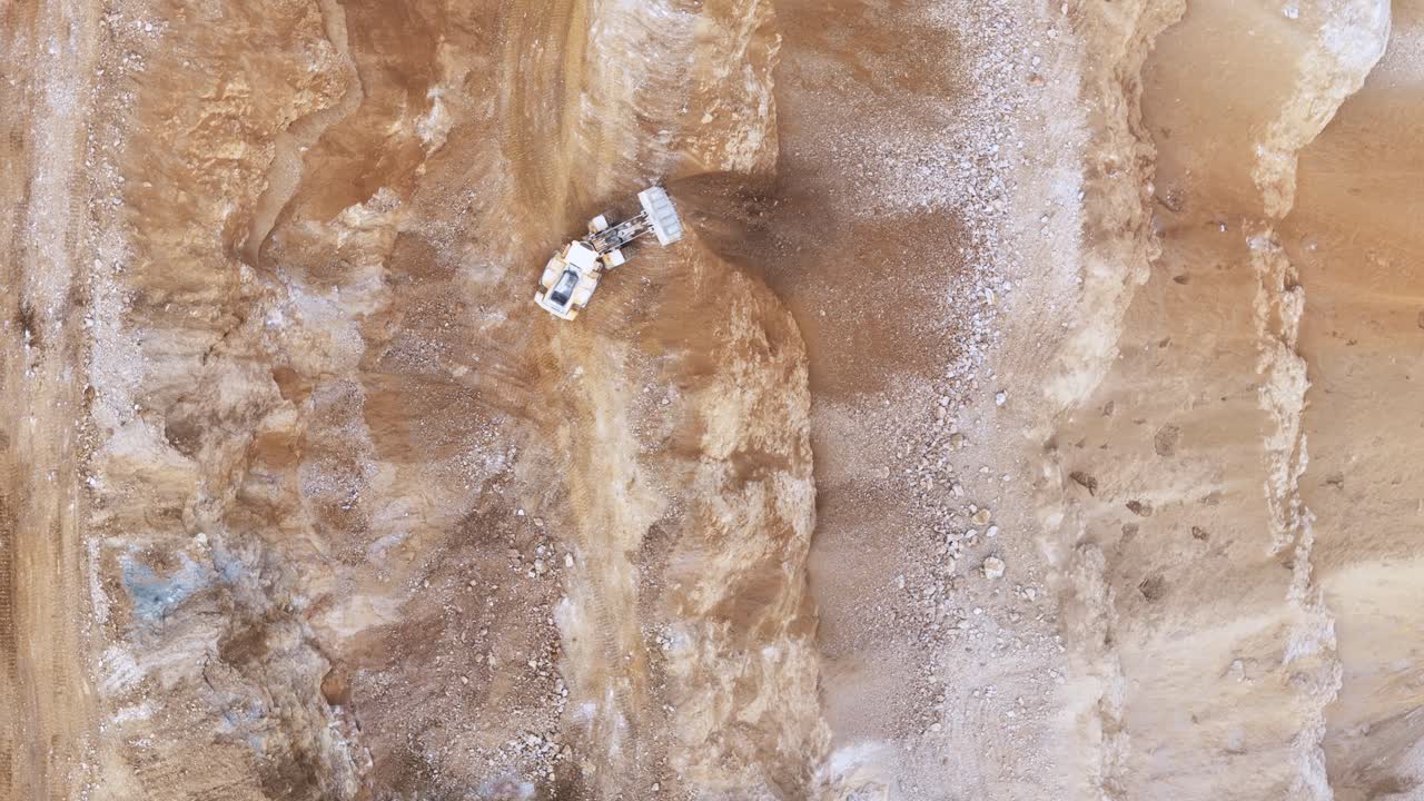 An Excavator Working on a Rugged Mining Site, Digging Through Layers of Soil and Rock to Extract Minerals From the Earth - Aerial Topdown Shot